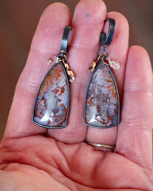 Close up of a pair of earrings with large, teardrop-shaped natural stone pendants, gold accents, and Herkimer diamonds held in hand.