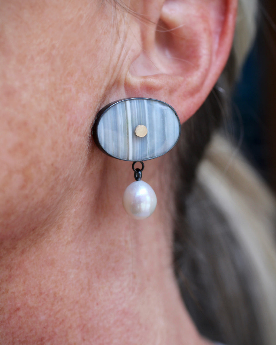 Oval banded agate earrings with vertical blue gray striping, centered 14k gold dot, and dangling white pearl drops in oxidized sterling silver.