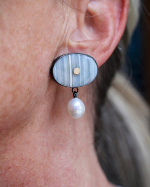 Close up of banded agate and pearl drop earrings worn on ear, showing soft striped stone, small gold accent, and luminous pearl movement.