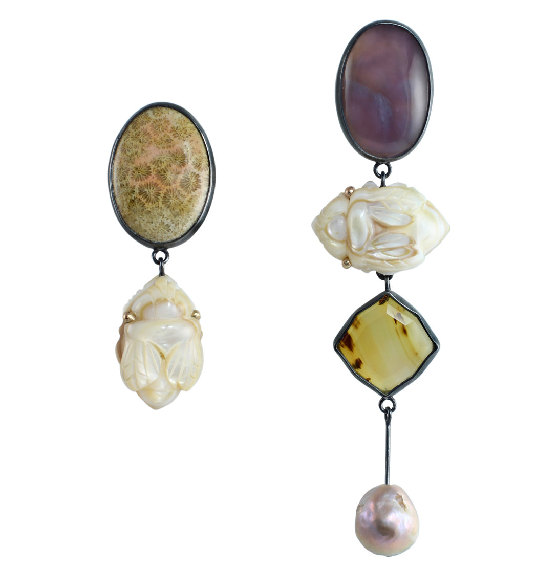 Asymmetrical gemstone drop earrings in oxidized silver and 14k gold featuring fossilized coral, smoky purple agate, carved mother of pearl bees, Montana agate, and a pearl drop on a white background.