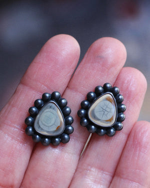 Imperial jasper all-seeing eye stud earrings in oxidized sterling silver resting in an open hand.