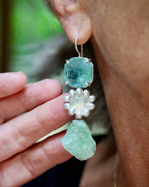 Close up of sterling silver earring with faceted aquamarine and raw green calcite photographed on model.