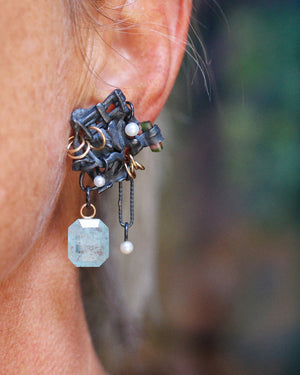 Close-up of a sculptural Fragment earring worn on the ear, with a dangling aquamarine, small pearls, gold rings, and a watermelon tourmaline crystal.