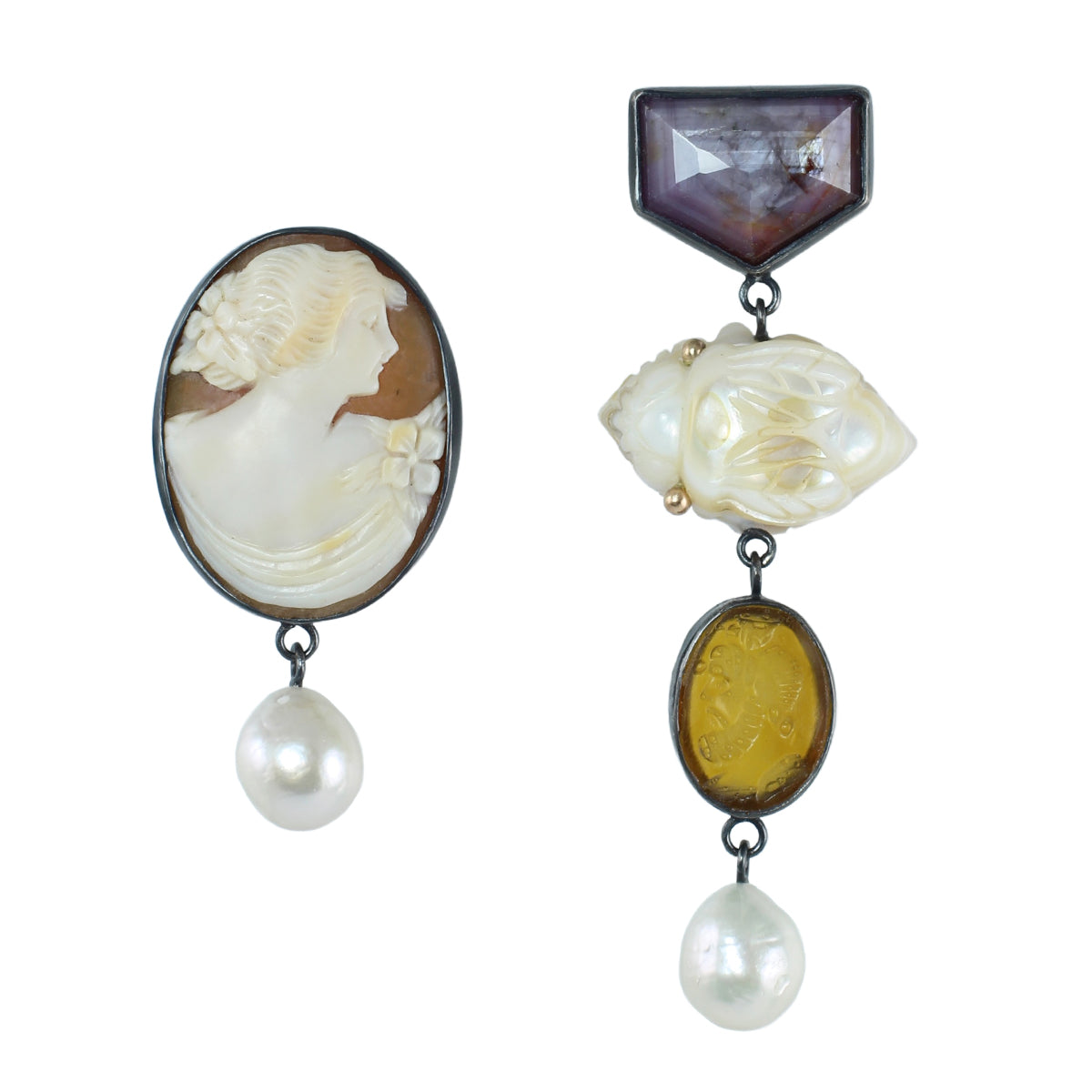 Asymmetrical drop earrings in oxidized silver and 14k gold featuring an antique shell cameo, pink sapphire, carved mother of pearl, golden intaglio, and freshwater pearl drops on a white background.