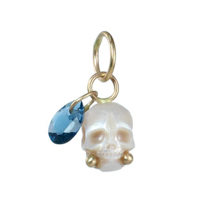 A skull charm with gold details, featuring a small blue faceted teardrop gemstone and gold ball accents on the cheeks, shown on a plain white background.