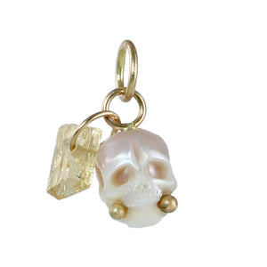Pinkish white carved pearl skull with gold accents and small imperial topaz skull on a white background.