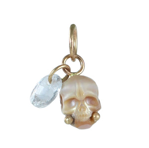 A carved pearl skull charm with gold accents and faceted oval pale blue gemstone dangle photographed on white. 