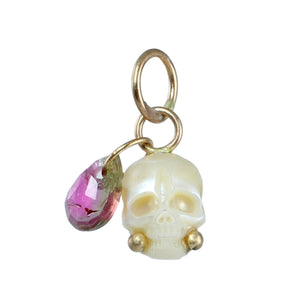 A carved pearl skull charm with gold  accents, and a dangling bright pink and green faceted gemstone teardrop on a plain white background.