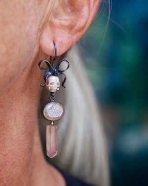 Calavera earring worn on the ear with a carved pearl skull, oxidized silver bow, opalized druzy, pink lithium quartz, and 14k gold accents.