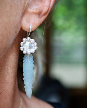 Close up of sterling silver earring with carved soft blue chalcedony leaf photographed on model.