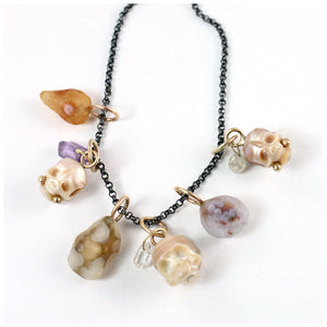Six handcrafted charms featuring three with carved pearl skulls with gemstone and gold accents and three with colorful Gobi Desert agates shown together on an oxidized silver chain laying on a white background.