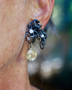 Close-up photo of a Fragments earring worn on the ear, with fused oxidized sterling silver, pearls, gold accents, and a large round faceted citrine drop. Shows movement and scale. 