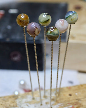 Hand forged sterling silver cocktail picks standing upright, each topped with a colorful phantom agate stone.