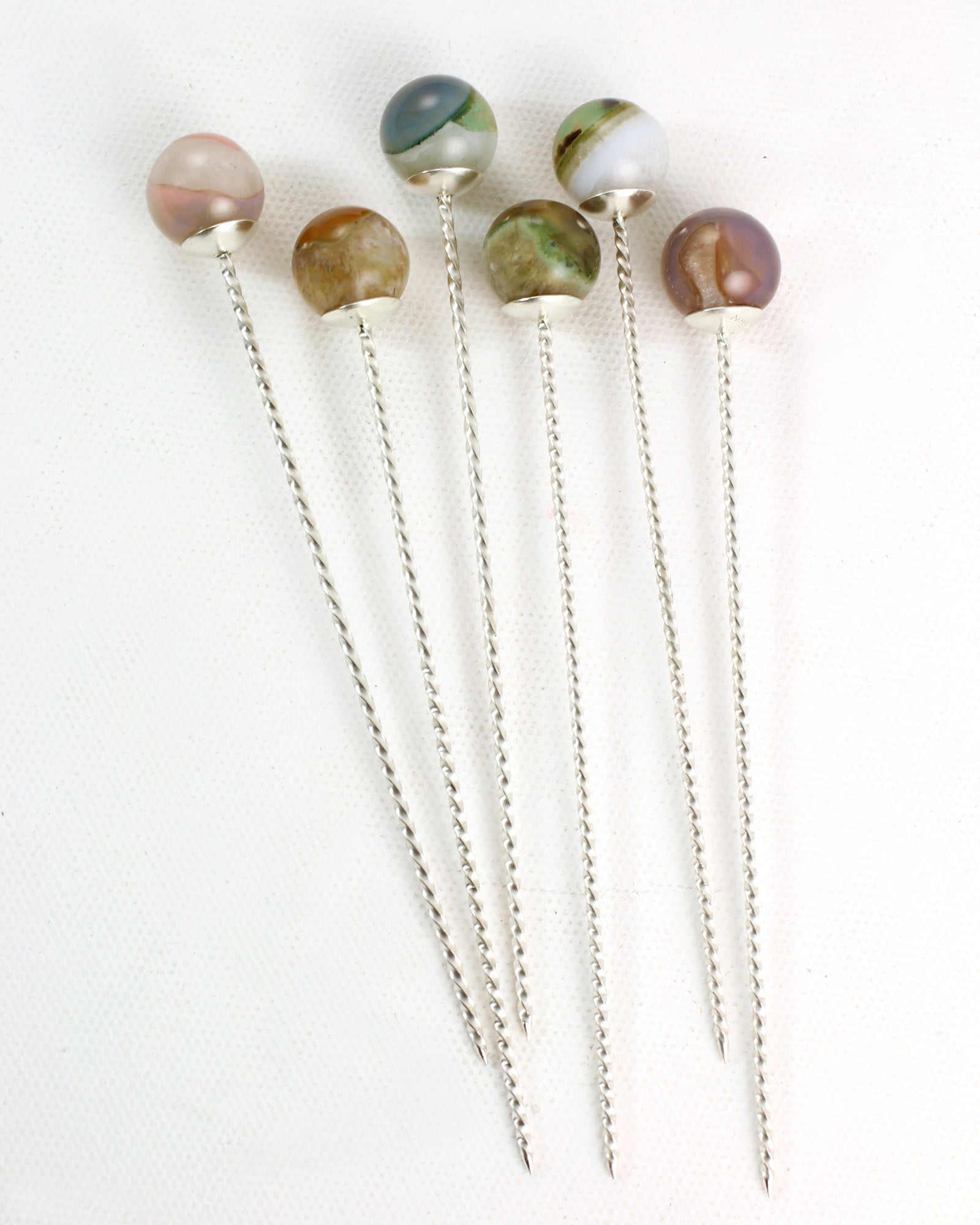 Set of six sterling silver cocktail picks with twisted wire stems and colorful phantom quartz tops on a white background.
