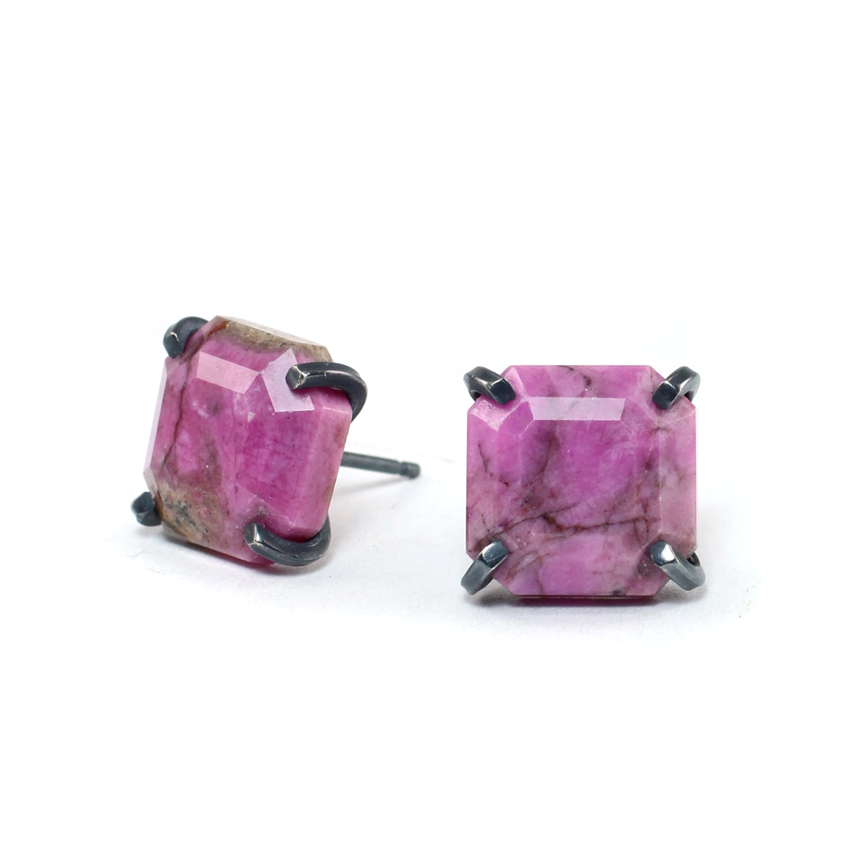 Close-up of square pink cobalto calcite stud earrings with natural dark inclusions and faceted surfaces, secured by four oxidized sterling silver prongs on a white background.
