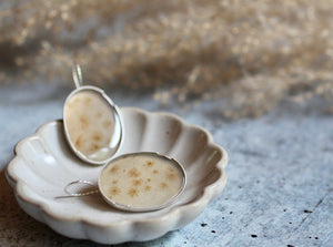 Oval dendritic agate earrings in a ceramic shell dish, showing natural earthy inclusions and matte silver.