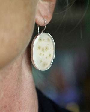 Handmade oval dendritic agate earrings with natural branch-like patterns and matte finished sterling silver settings worn.