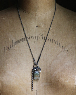 One-of-a-kind green sunstone necklace displayed on a vintage dress form, with oxidized sterling silver chain, pearls, collected fragments and dangling crystal chain.
