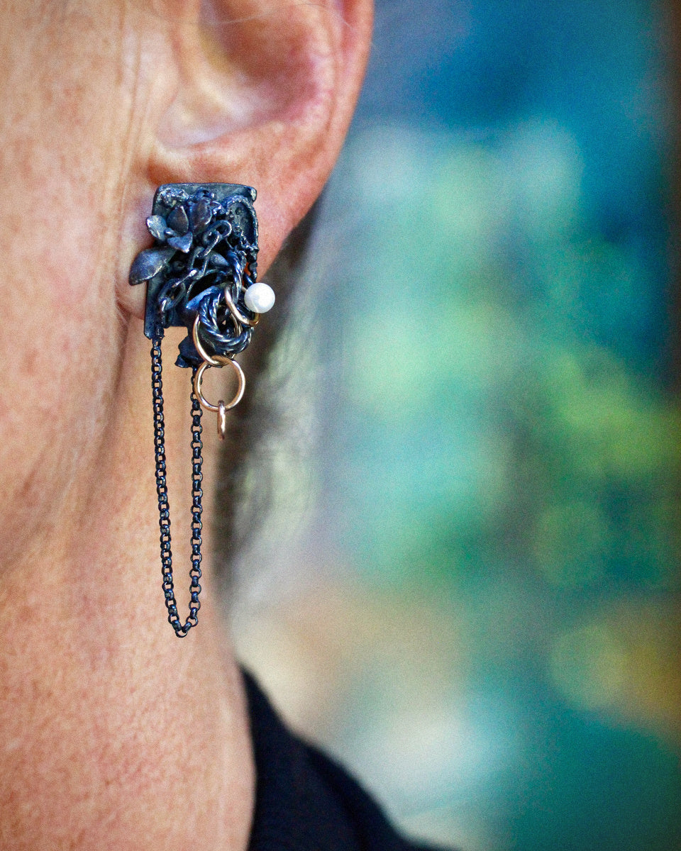 Asymmetrical Fragment earrings in textured oxidized sterling silver with 14k gold fill rings, white pearls, dangling chains, and a teardrop dendritic agate with branching black and brown inclusions photographed floating on a white background.