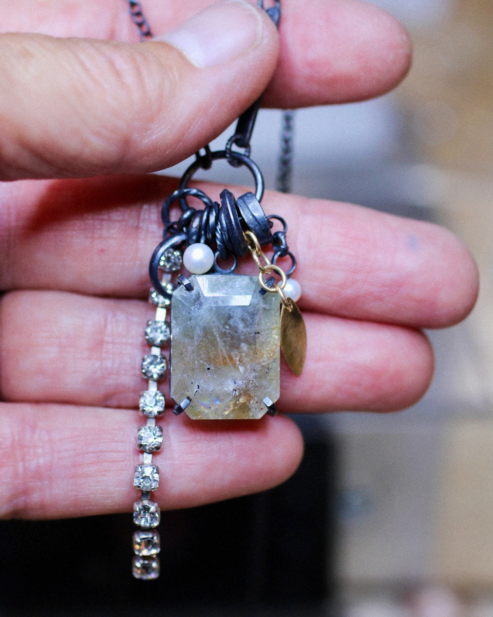 One-of-a-kind green sunstone necklace on a white background with pearls, oxidized sterling silver, collected fragments and a dangling length of crystal chain.