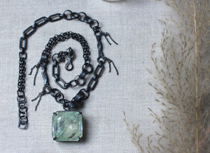 Large garden quartz necklace with oxidized sterling silver mixed link chain resting on textured fabric beside soft dried grasses.