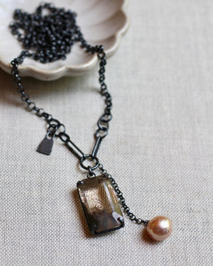 Rutile quartz and baroque pearl long necklace in oxidized sterling silver resting on linen.