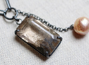 Macro detail of rutile quartz gemstone with earthy mineral inclusions in a dark silver prong setting.