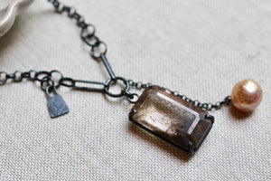 Close view of faceted rutile quartz with brown and grey inclusions and a baroque pearl chain drop.