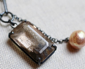 Macro detail of rutile quartz gemstone with earthy mineral inclusions in a dark silver prong setting.