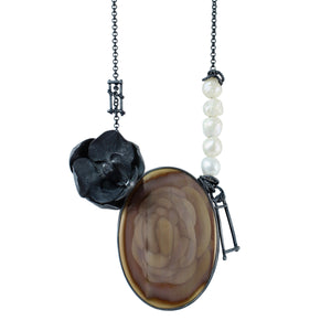 Close-up of a large mauve and brown imperial jasper with concentric rosette patterns, a dark oxidized silver orchid, irregular white pearls, and handmade ladder-like silver fragments. Photographed floating on a white background.