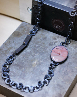 Close-up of imperial jasper necklace with handcrafted oxidized chain and gold accents resting on metal surface, highlighting botanical tab detail.
