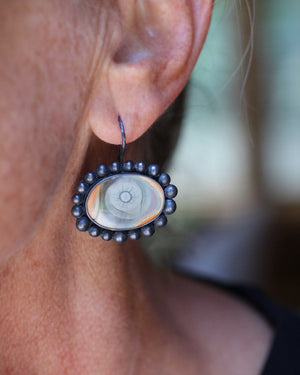 Close-up of one Imperial jasper eye earring worn on the ear, with pale green, cream, peach, and gray tones framed in oxidized silver.