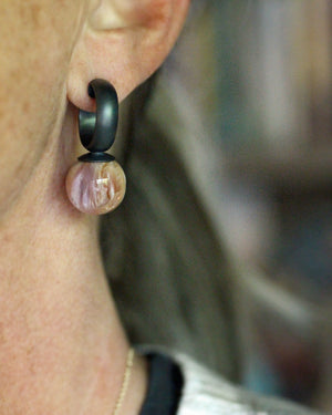 Natural shell hoop earring worn on the ear, showing a dark oxidized silver hoop and softly patterned shell drop.