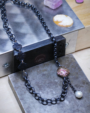Handmade mixed chain oxidized silver and gold necklace sitting on jewelers bench featuring pink cobalt calcite centerpiece set in gold and pearl drop detail