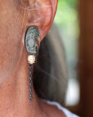 Close-up of a colorful imperial jasper and carved pearl skull earring worn on the ear, with a long oxidized sterling silver chain drop.