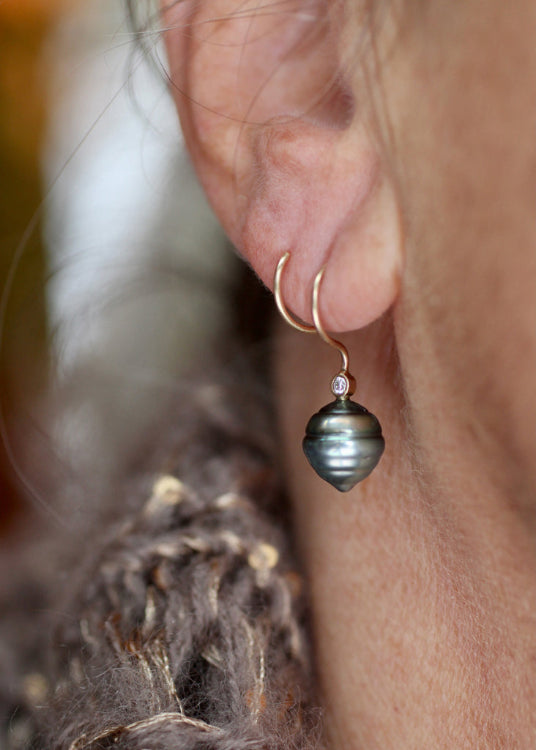 Close-up of an earring with a diamond and Tahitian pearl worn by a person.