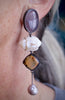 Asymmetrical gemstone drop earrings in oxidized silver and 14k gold featuring fossilized coral, smoky purple agate, carved mother of pearl bees, Montana agate, and a pearl drop worn.