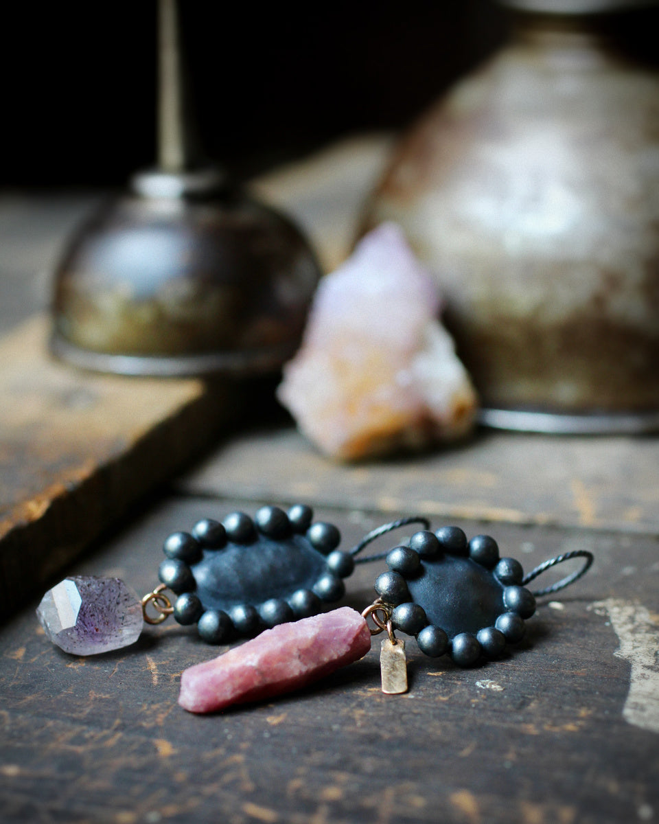 Mismatched raw ruby crystal and melody stone earrings shown on white, with oxidized sterling silver bauble settings and recycled 14k gold details.