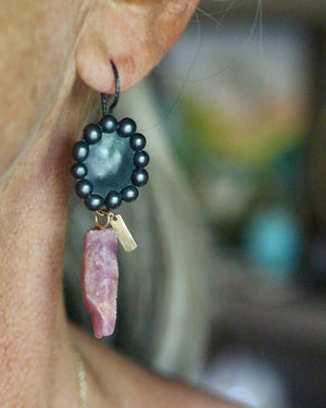 Single raw ruby crystal earring worn on the ear, with an oxidized sterling silver bauble setting and small recycled 14k gold accent.