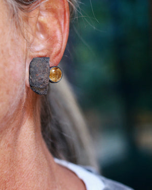 Rust and golden rutilated quartz stud earring worn on the ear, showing the scale and contrast of the raw rust and faceted gemstone.