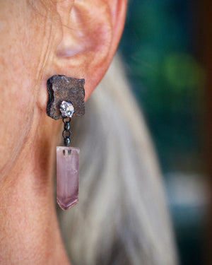 Close-up of an asymmetrical rust shard earring with a Herkimer diamond and dangling pale pink lithium quartz crystal worn on ear.