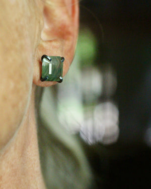 Square green rutilated quartz stud earring worn on the ear, set in a dark oxidized silver prong setting.