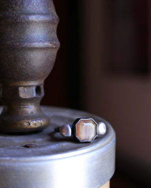 Golden sapphire ring with silver pearls set in oxidized sterling silver, resting on a worn metal surface with warm, moody lighting