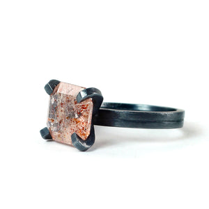 Faceted peach and copper sunstone ring with substantial oxidized sterling silver prongs and double band.