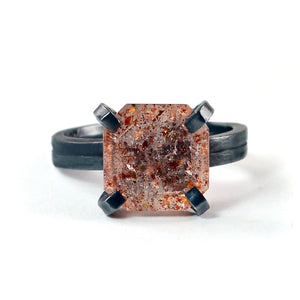 Square faceted sunstone with sparkling reddish copper inclusions, held by four bold oxidized sterling silver prongs.