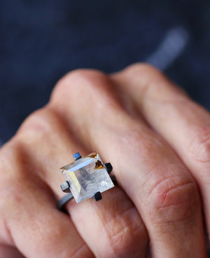 One-of-a-kind square white topaz ring with golden inclusions and oxidized sterling silver setting, shown worn on a hand.